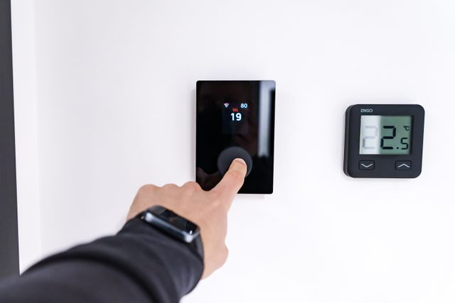 a hand adjusting a digital thermostat