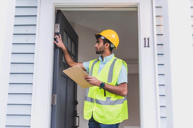 a-property-inspector-in-a-yellow-vest-and-hard-hat-looking-at-the-homes-doorway