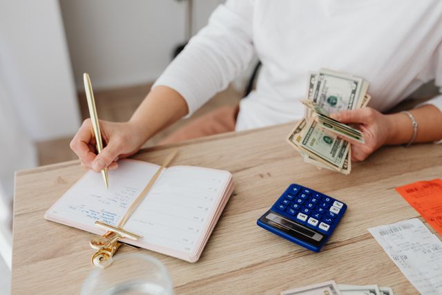 person holding cash and writing in a planner